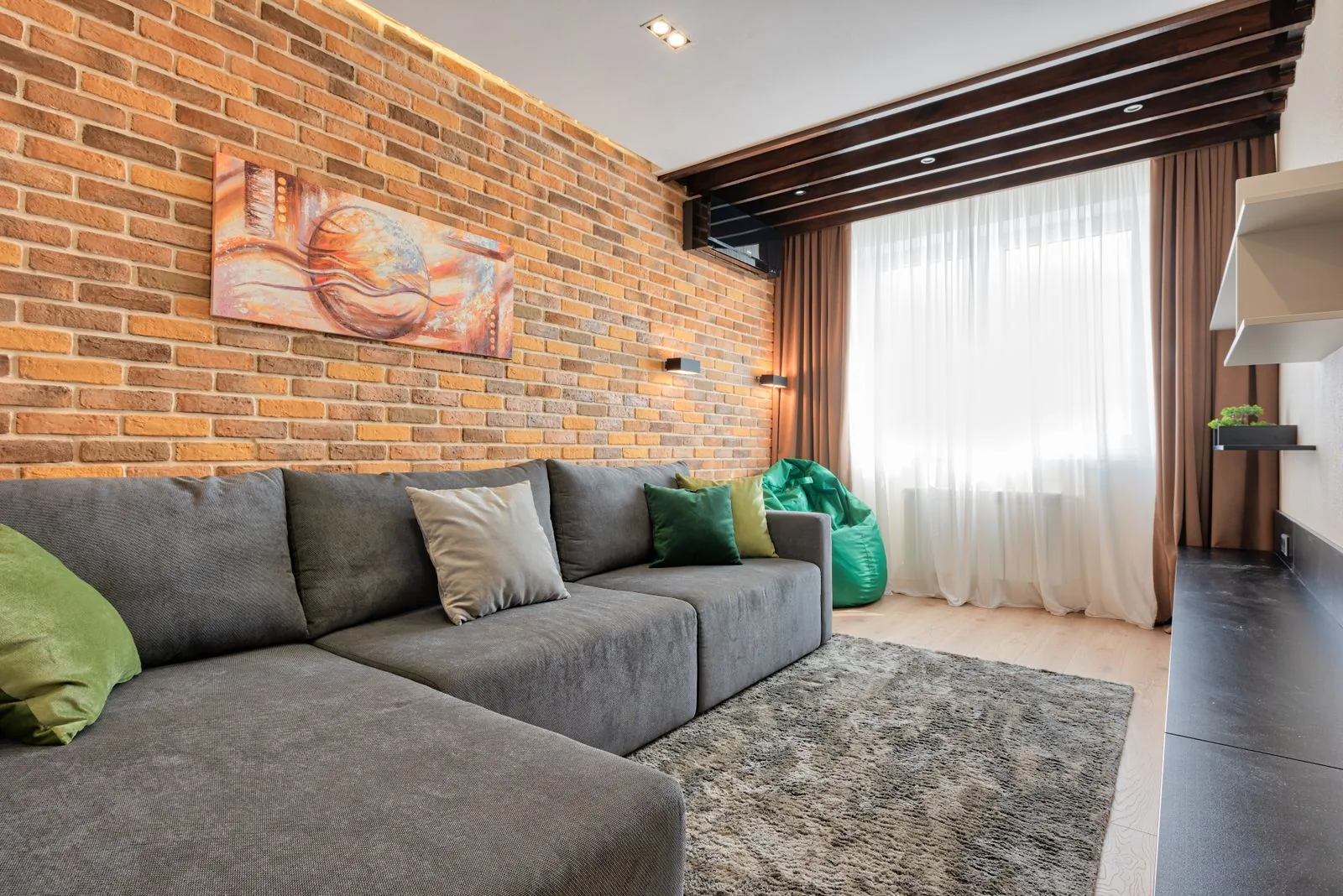 Ruang keluarga dengan sofa abu-abu dan AC di atas jendela.